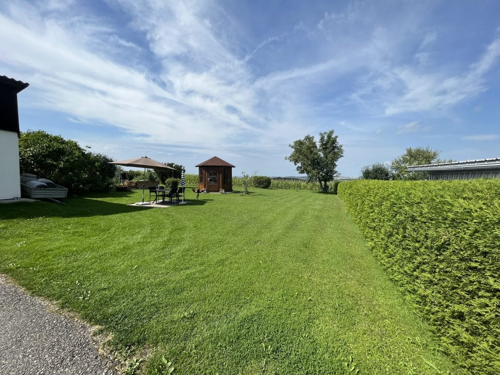 Ausgangssituation Zwei-Generationen-Garten. Große Rasenfläche, großer Nussbaum in der hinteren Ecke, Holzpavillon und Sonnenschirm mit Gartenmöbel